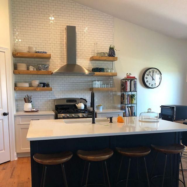 Modern kitchen with white island, dark stools, open shelves, and stainless range hood