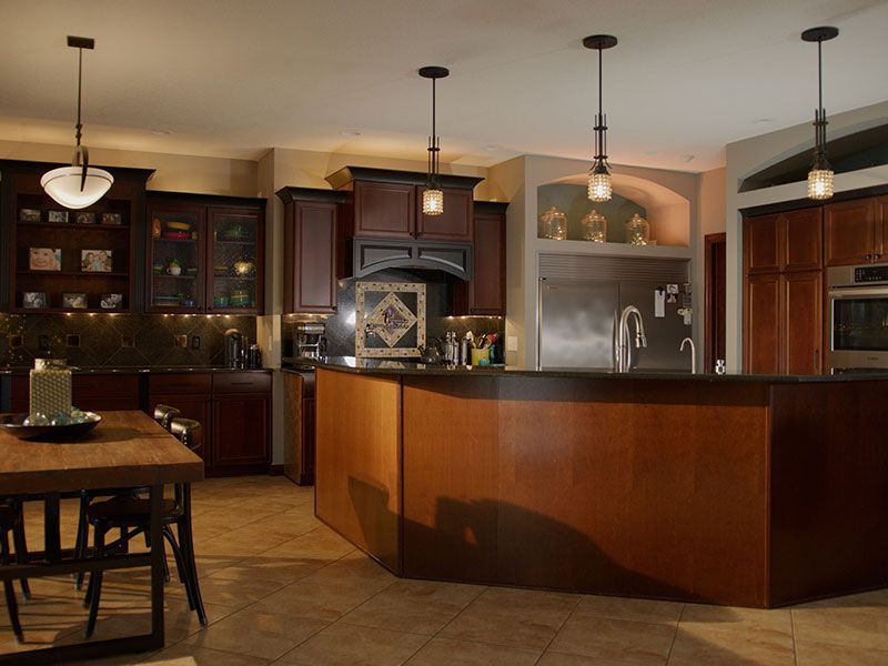 Modern kitchen with dark wood cabinets, curved island, pendant lights, and tiled floor