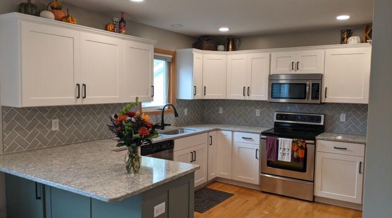 Bright kitchen with white cabinets, gray countertops, stainless stove, and a flower vase on the island