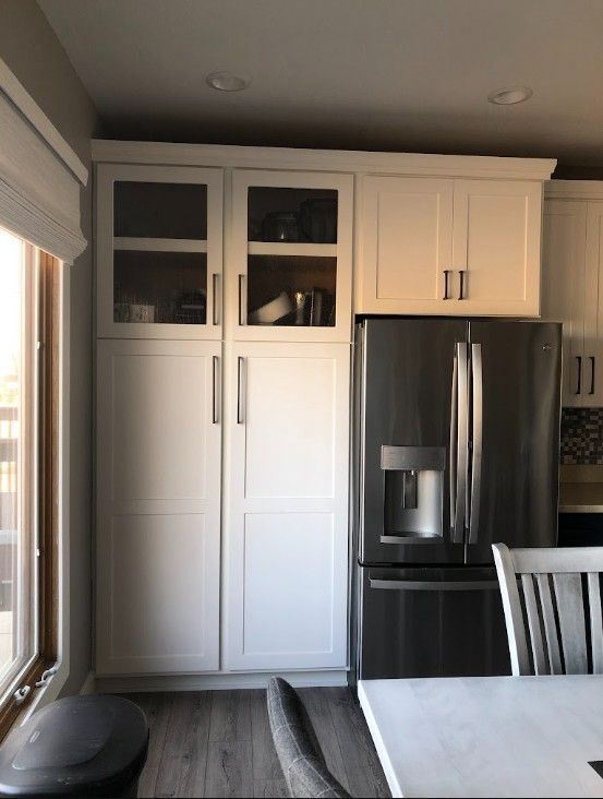 Modern kitchen with white cabinets, stainless steel fridge, and a dining table by a window.