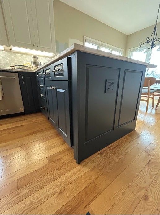 Black kitchen island with cabinets and wood flooring in a bright modern kitchen
