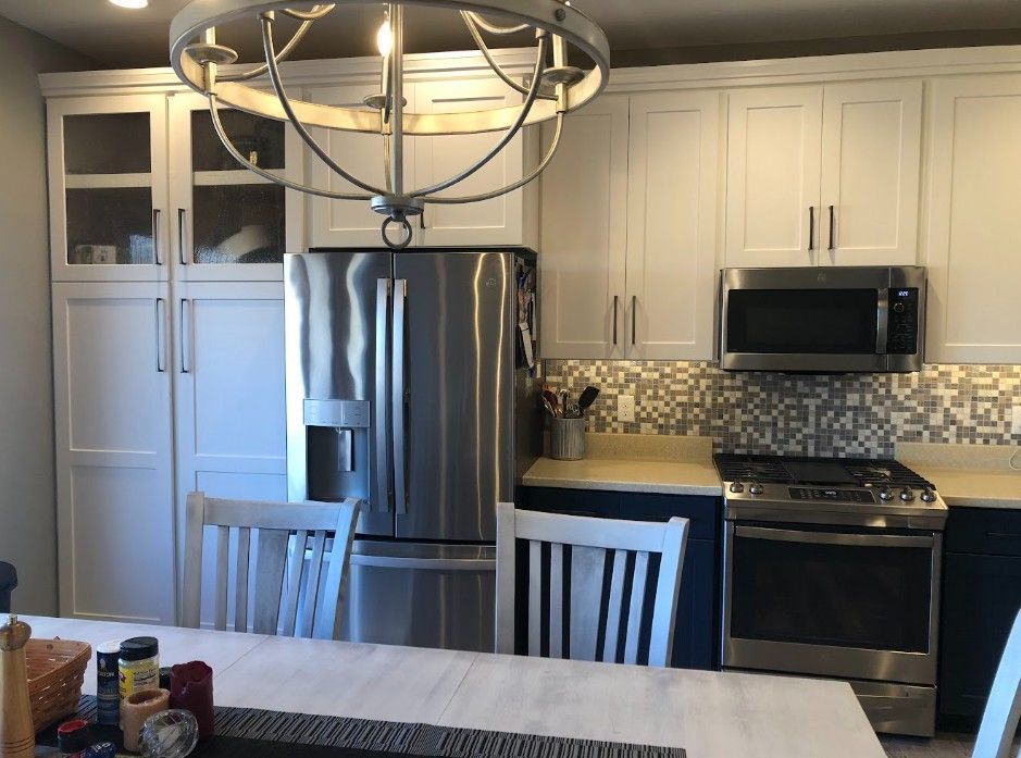 Modern kitchen with stainless steel appliances, white cabinets, mosaic backsplash, and dining table in foreground