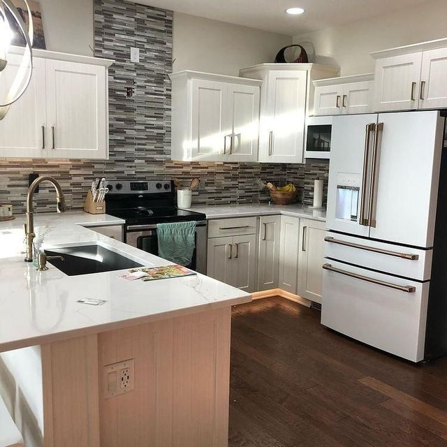 Bright modern kitchen with white cabinets, stainless appliances, stone backsplash, and dark wood floors