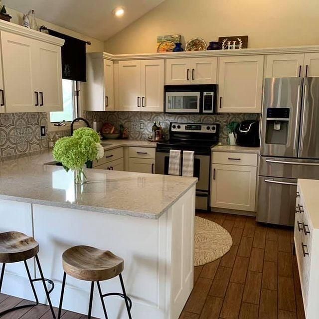 Bright white kitchen with island, stainless steel appliances, wood floor, and two stools