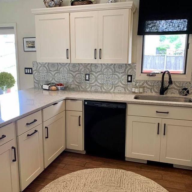 Modern kitchen with cream cabinets, patterned backsplash, black dishwasher, and window above the sink.