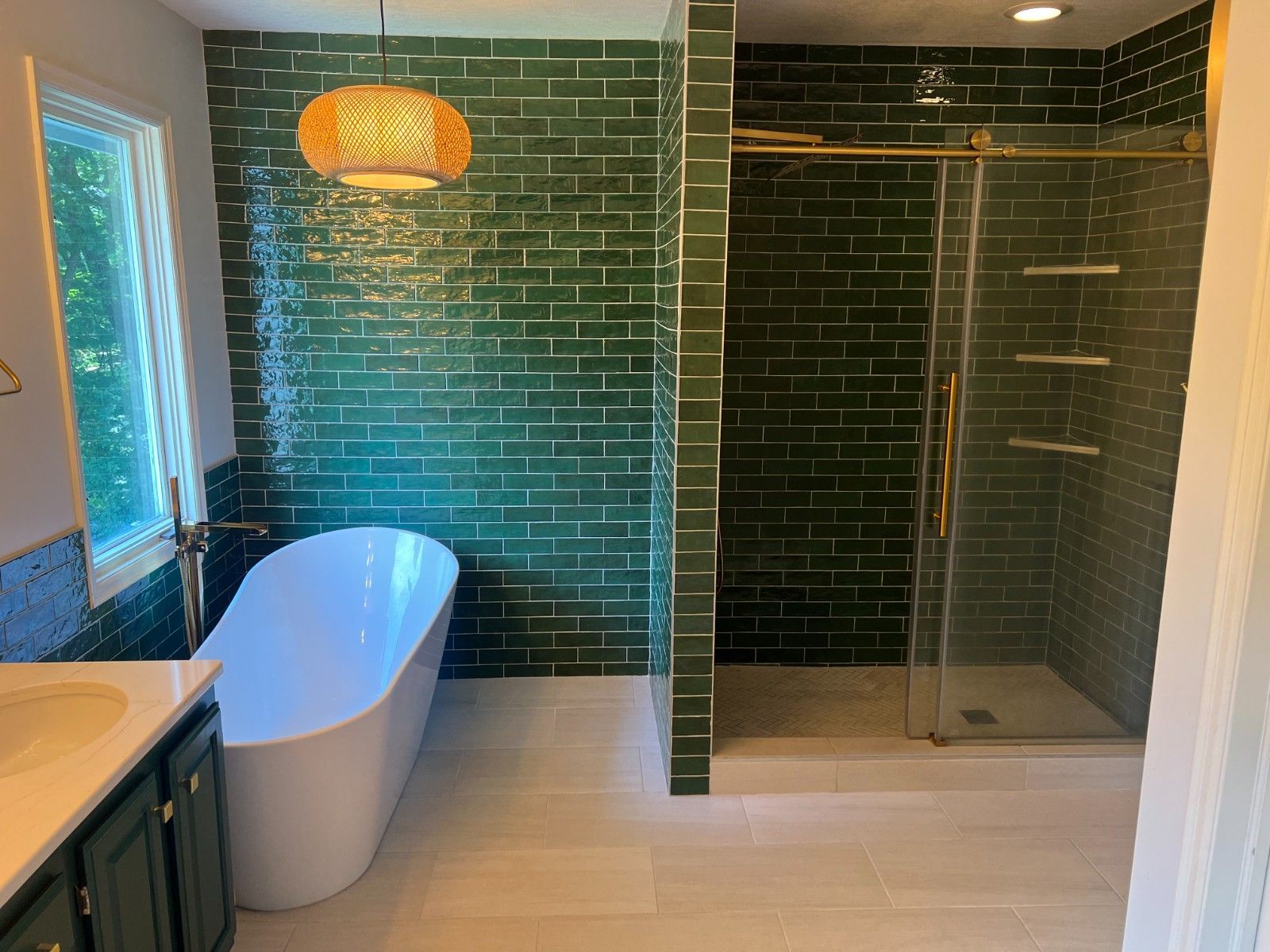 Modern bathroom with green tile wall, freestanding tub, double vanity, and glass shower.