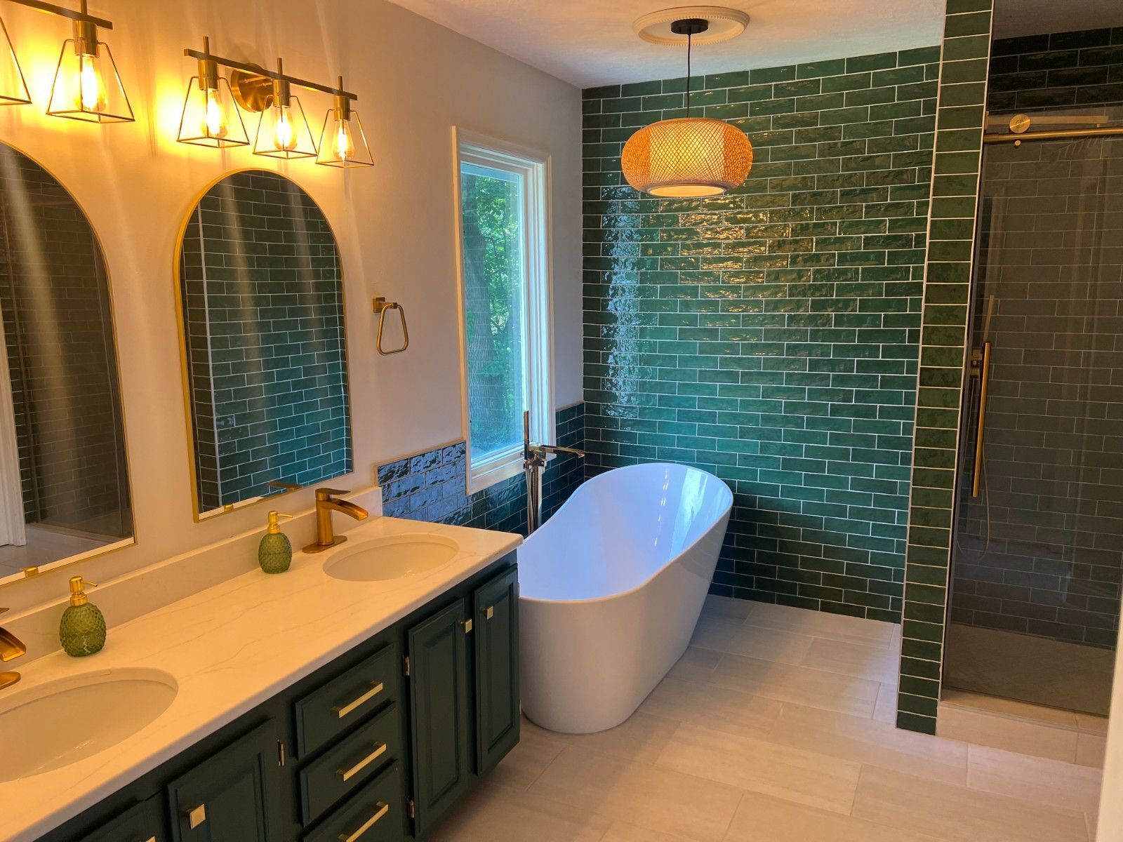 Stylish bathroom with green tile accent wall, freestanding tub, and double vanity under warm lighting