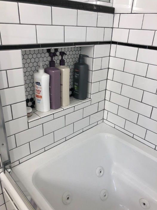 Built-in bathtub alcove with white subway tile and three bath product bottles on a recessed shelf