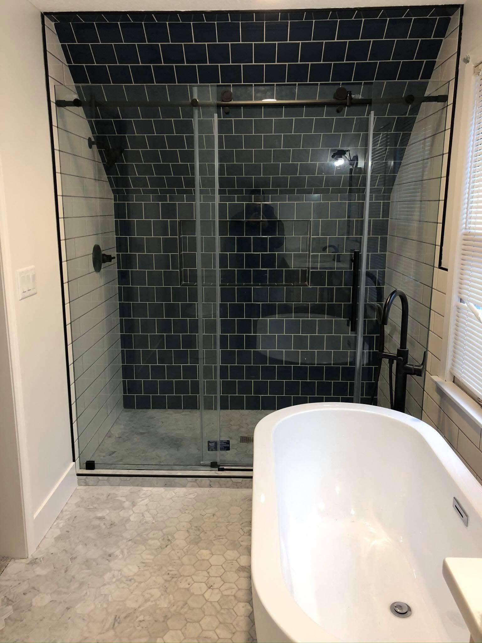 Modern bathroom with black-tiled walk-in shower and white freestanding bathtub