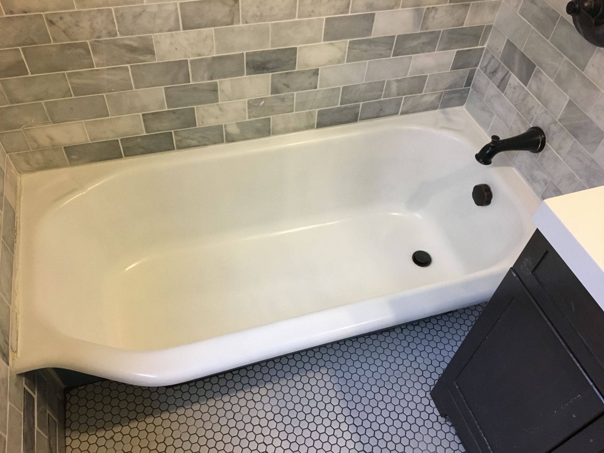 Empty white bathtub with black fixtures in a tiled bathroom