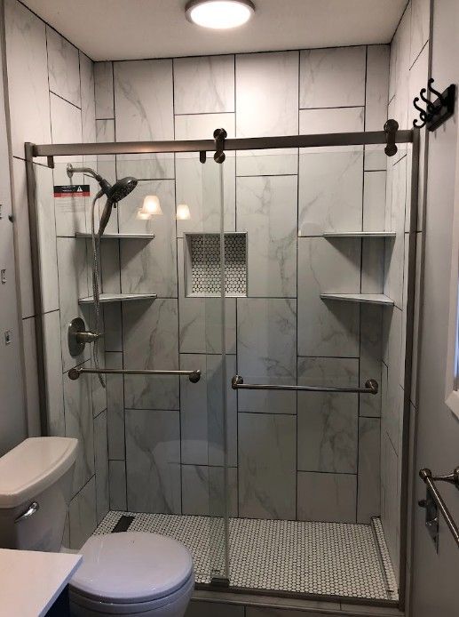 Accessible shower with bench, grab bars, tiled walls, and toilet in a small bathroom