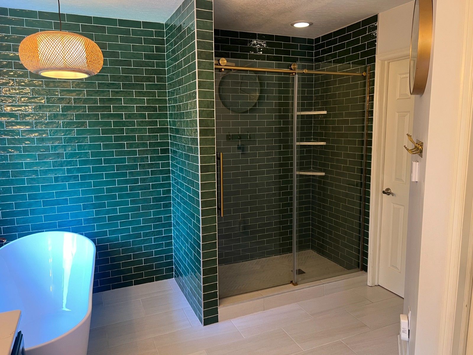 Modern bathroom with green tile walls, glass shower enclosure, and a glowing blue bathtub area.