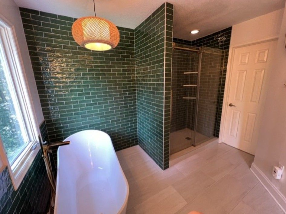 Modern bathroom with green tile walls, white tub, walk-in shower, and hanging pendant light.