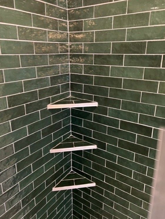 Green tiled corner shower with three white corner shelves and a built-in soap dish.