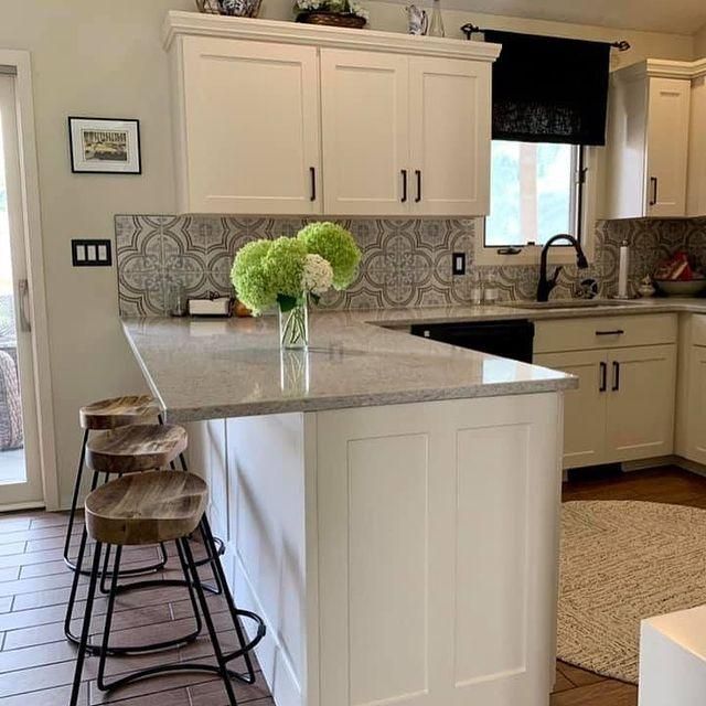 Bright kitchen with white cabinets, patterned backsplash, island stools, and a vase of green flowers