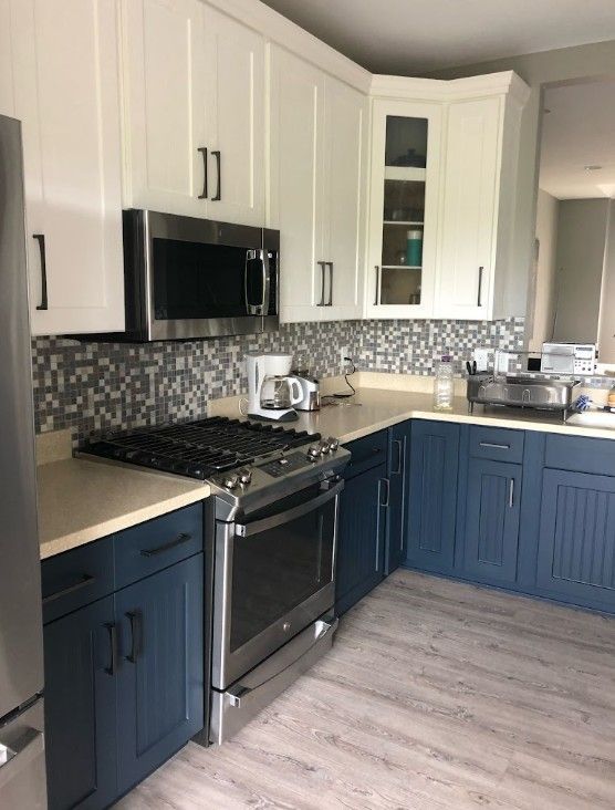 Modern kitchen with white upper cabinets, navy lower cabinets, black stove, and mosaic tile backsplash.