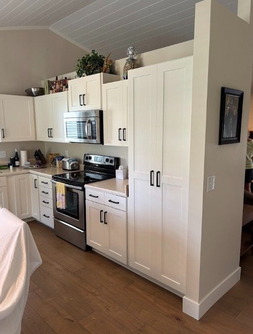 Bright white kitchen with stainless steel appliances, cabinets, and wood floors in a home interior