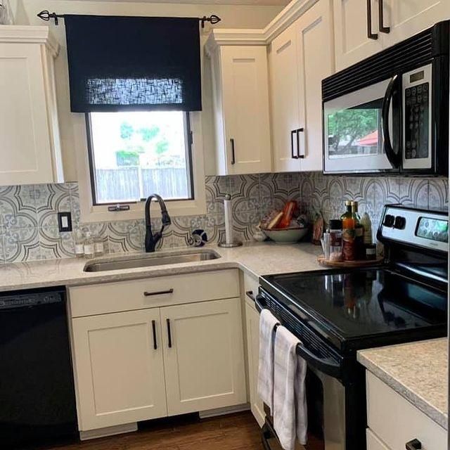 Bright kitchen with white cabinets, black appliances, sink under window, and black stove with towels hanging