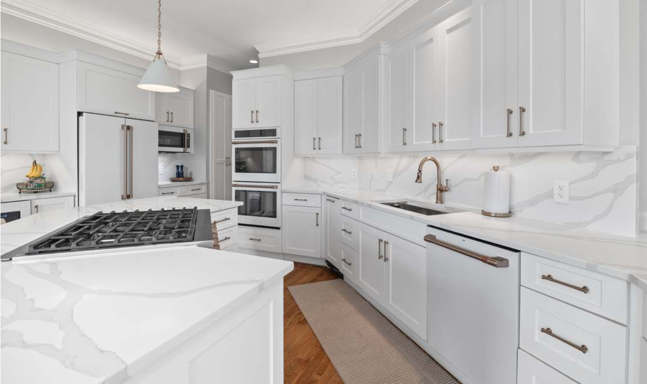 Bright white modern kitchen with marble countertops, gas range, double ovens, and large island
