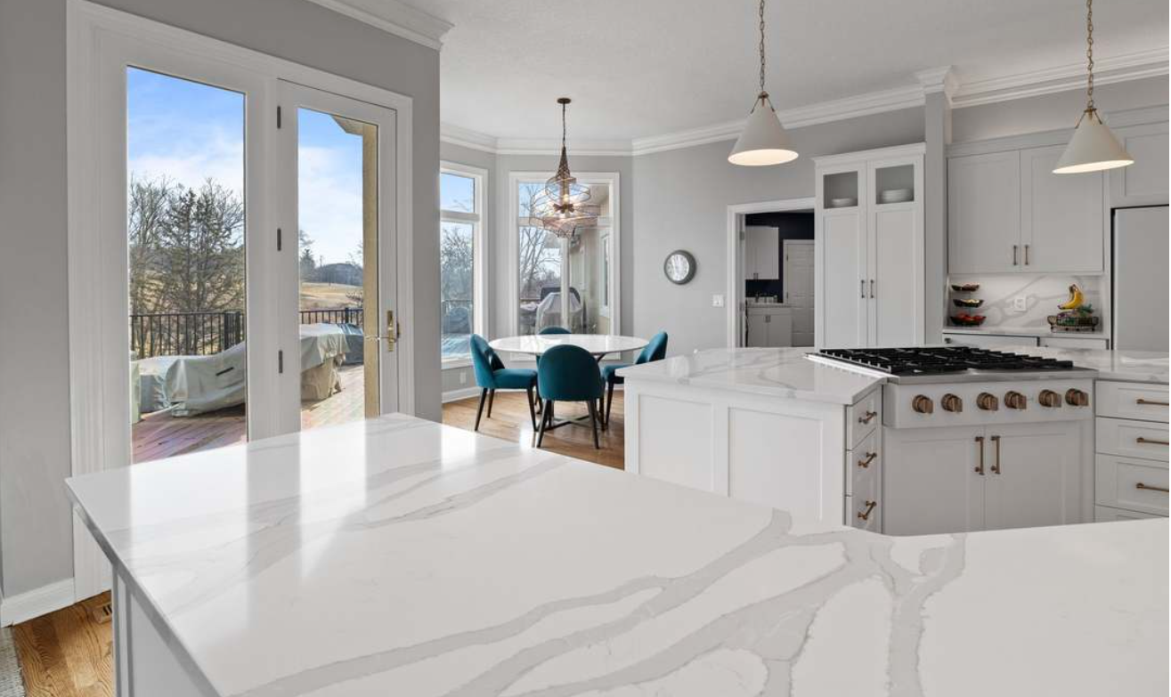 Bright white modern kitchen with island, dining area, and large glass doors to a deck and trees