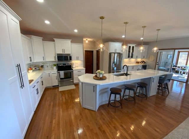 Bright modern kitchen with white cabinets, large island, stainless appliances, and hardwood floors