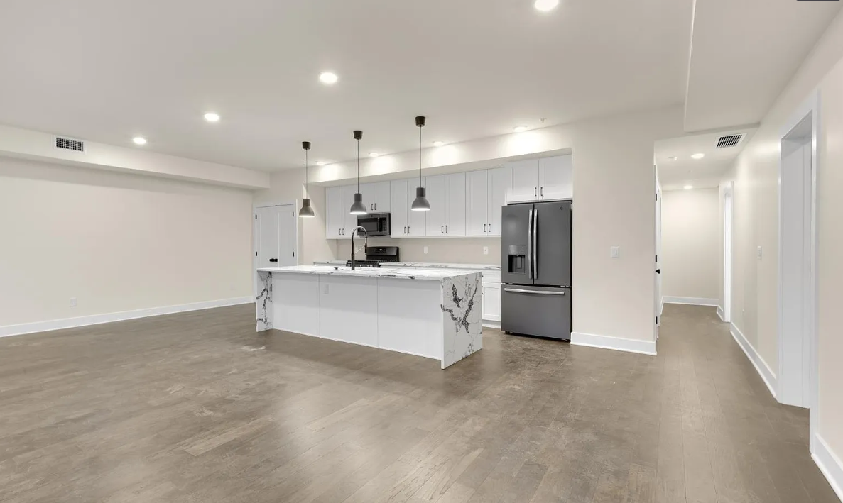An empty kitchen with a large island and a refrigerator