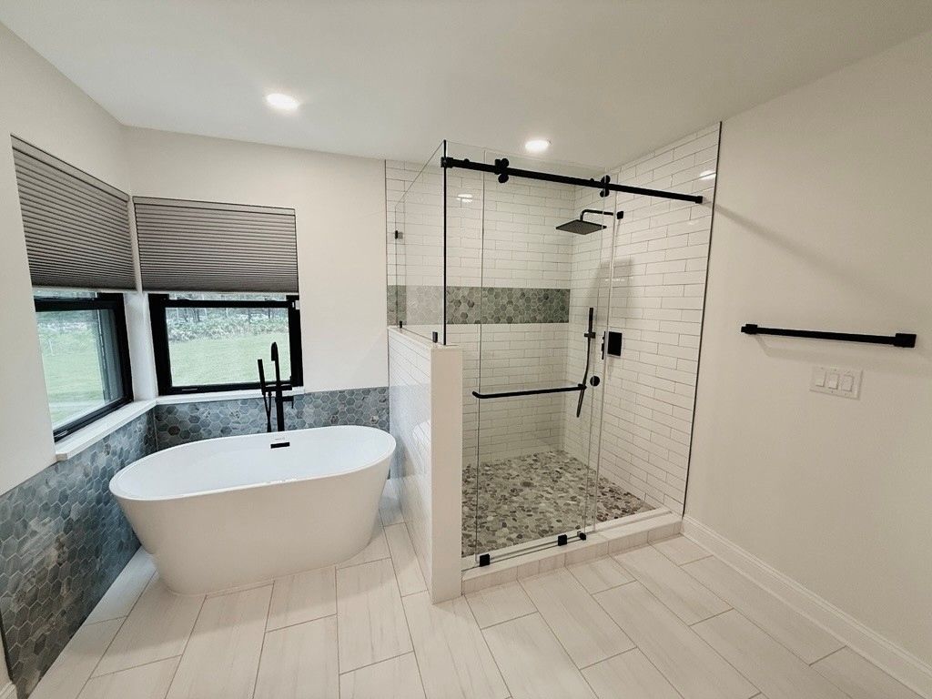 Bathroom with white subway tile shower, dark fixtures, and circular mirror.