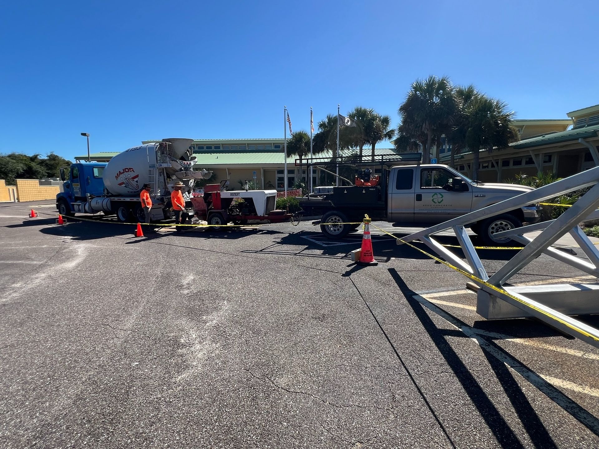 Concrete truck and pickup truck parked near a building. Workers in orange vests are present. Construction site.