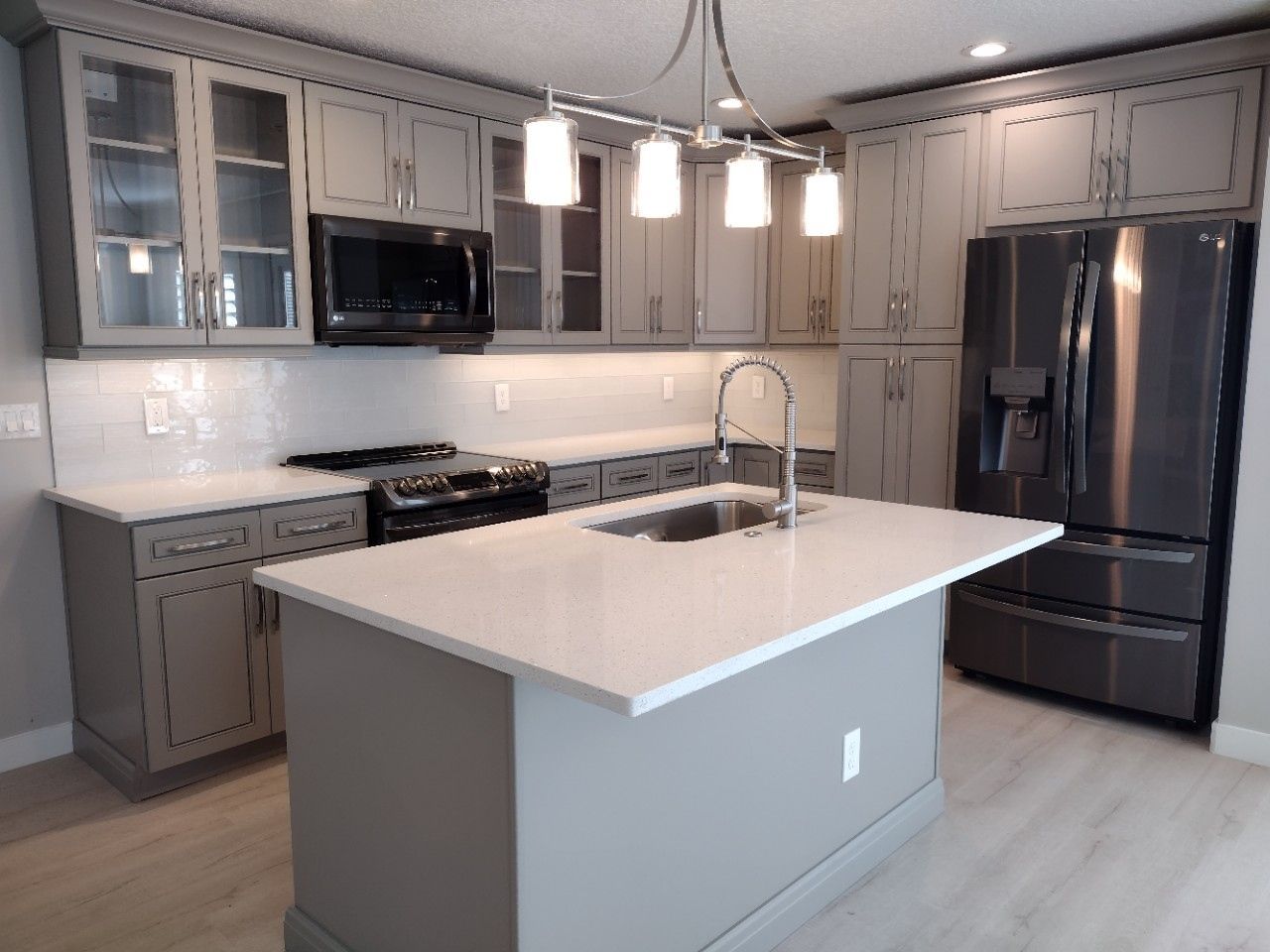 Gray kitchen with island, cabinets, white countertops, and stainless steel appliances.