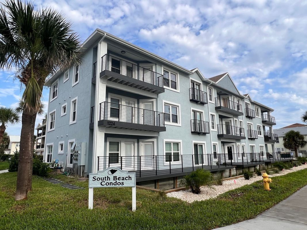 Light blue apartment building with balconies and a South Beach sign near palm trees under a cloudy sky