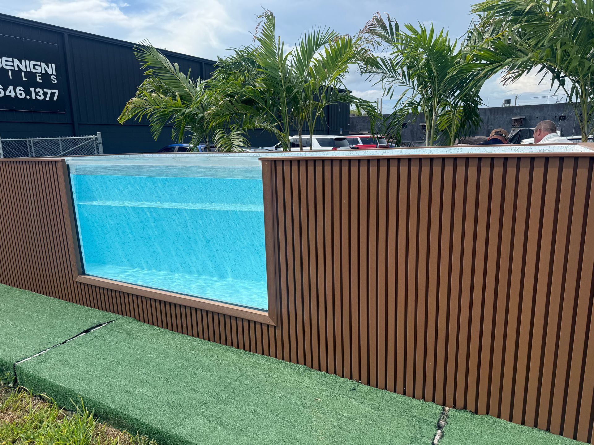 Outdoor pool with blue water, wooden privacy panels, and palm trees under a sunny sky