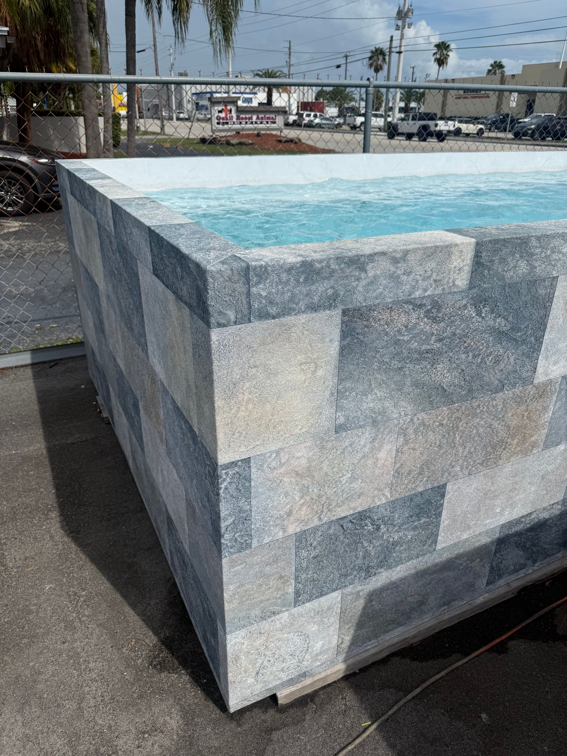 Stone-clad rectangular fountain with turquoise water outdoors near a waterfront promenade