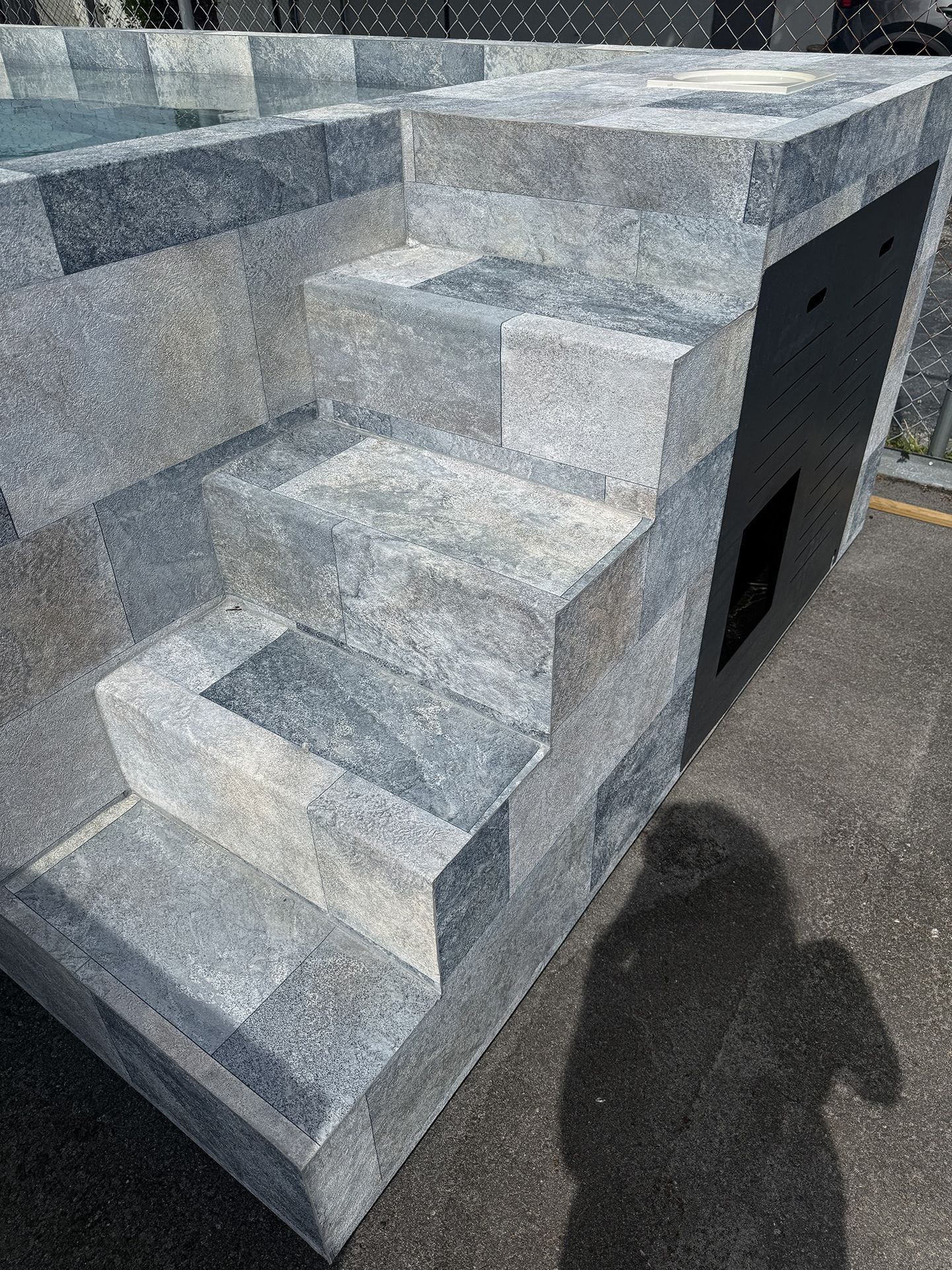 Gray granite steps on a stone platform beside a black utility opening outdoors