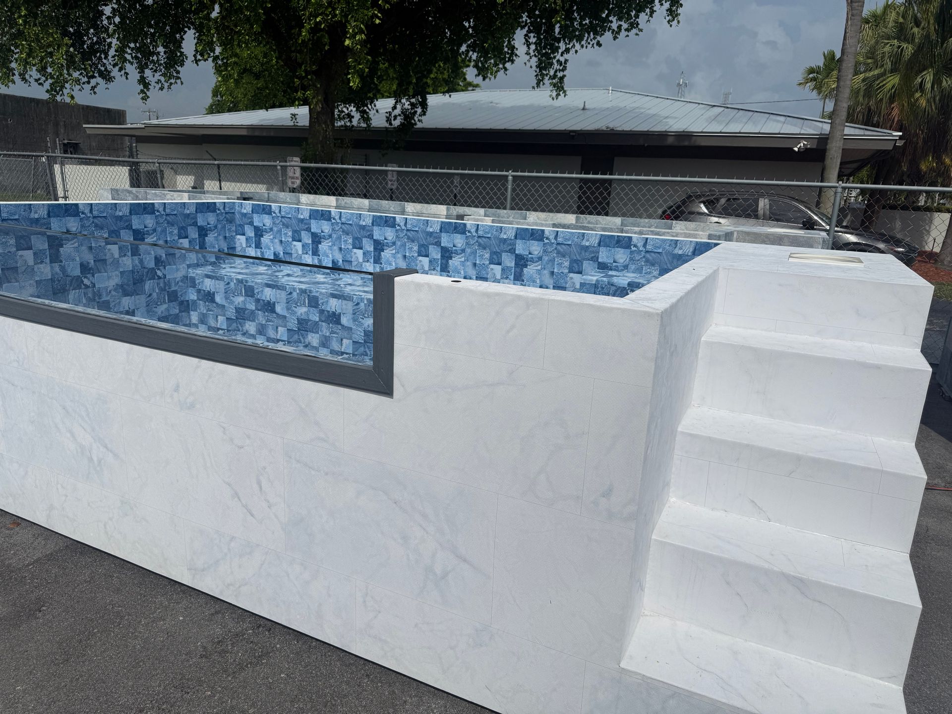Small blue-tiled pool with white stairs and walls outdoors beside a building