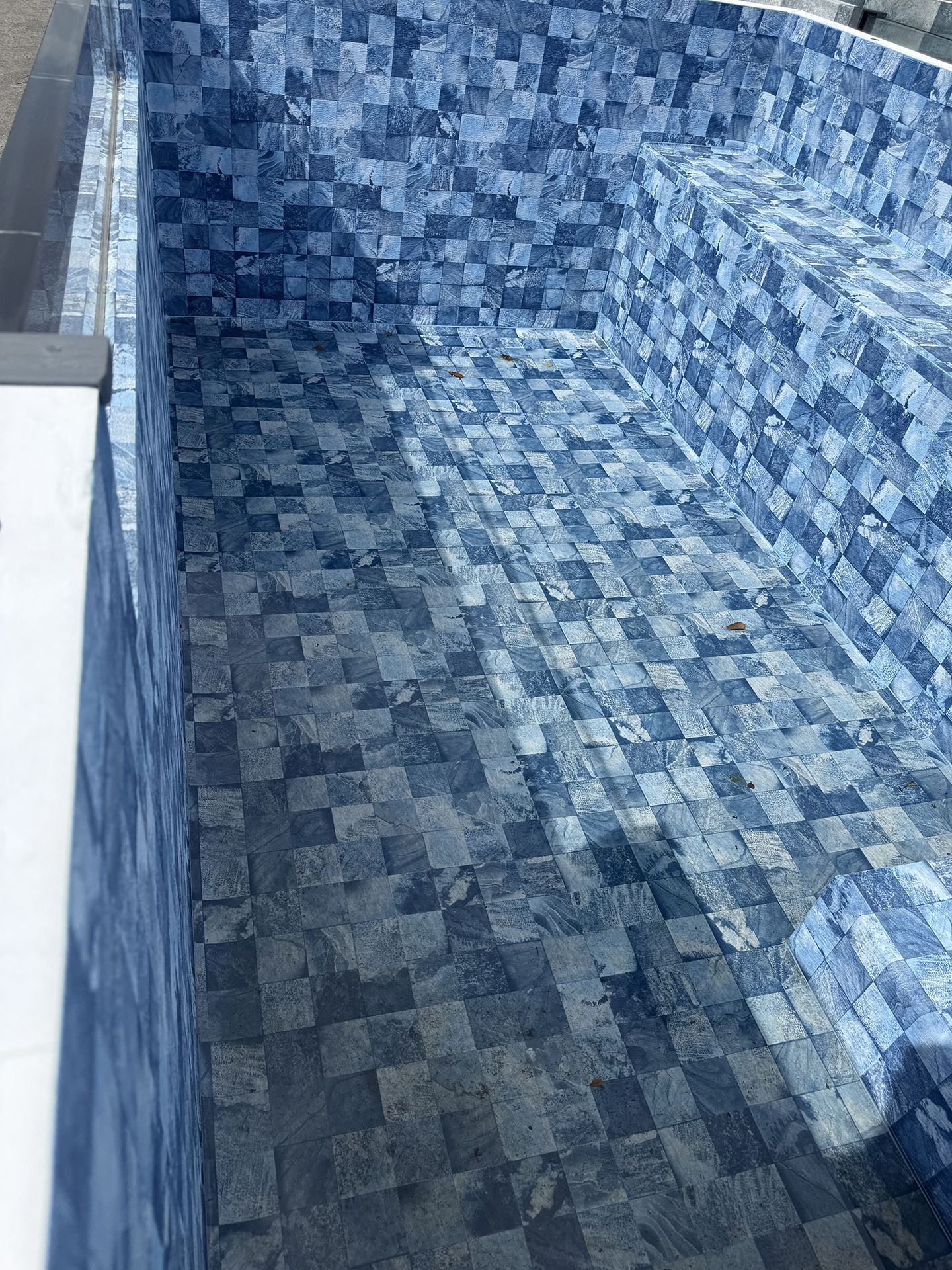 Empty blue-tiled swimming pool interior with a shallow ledge and sunlight shadows