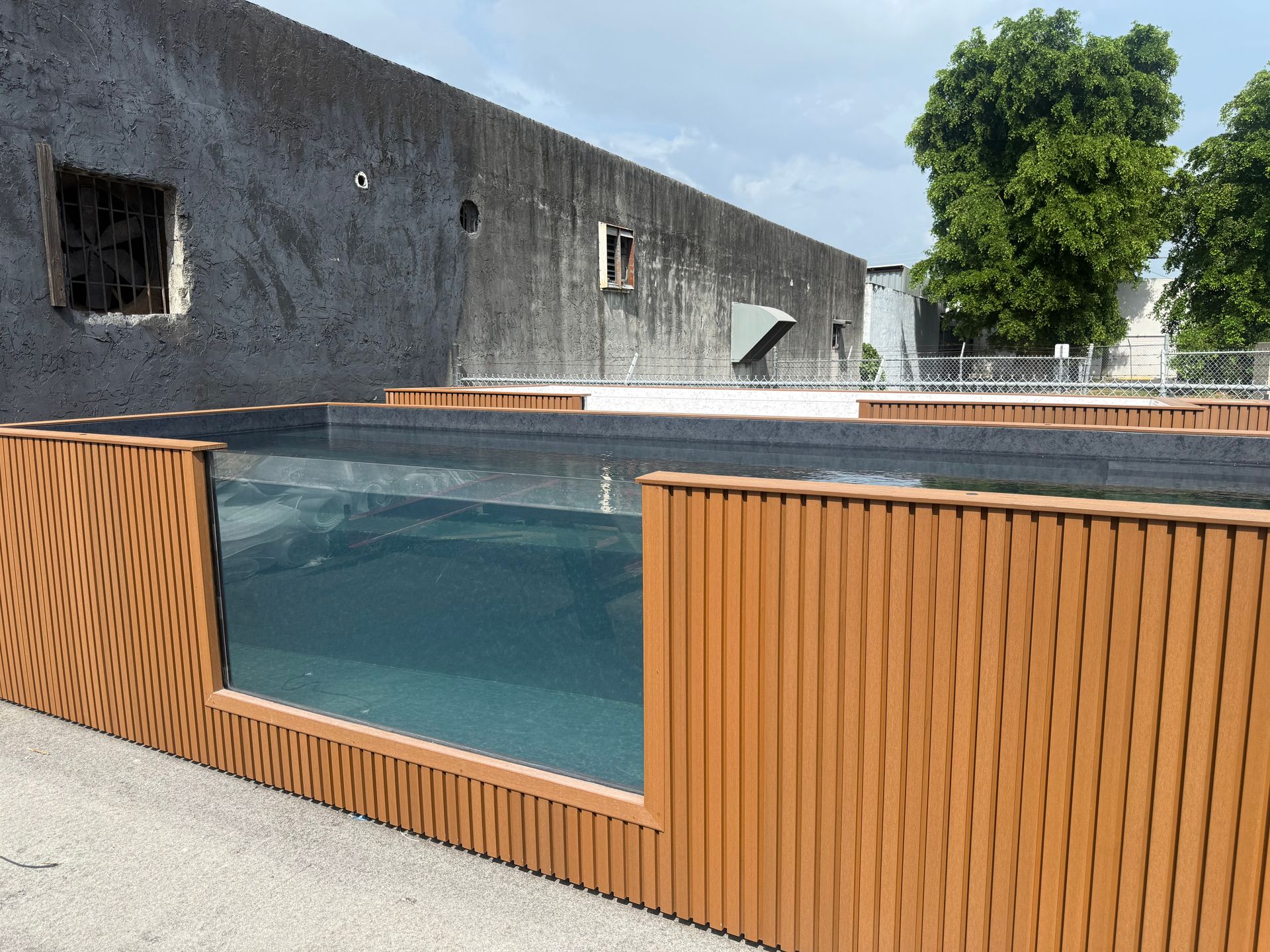 Modern pool with clear water, wood-paneled exterior, gray wall, and a tree in the background