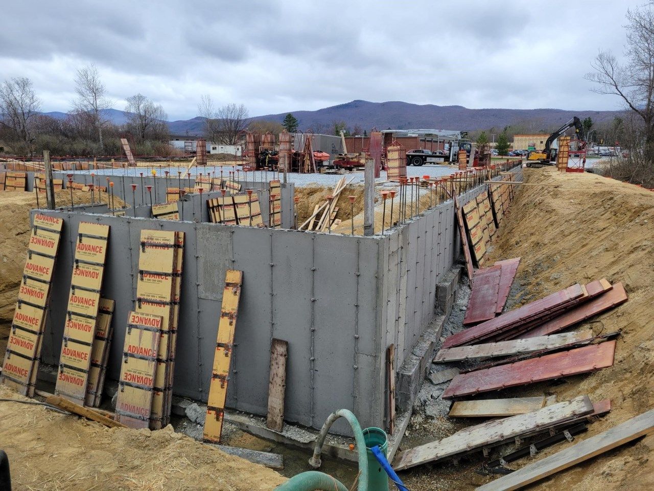 Construction site with concrete foundation walls, wooden forms, and earth berms.