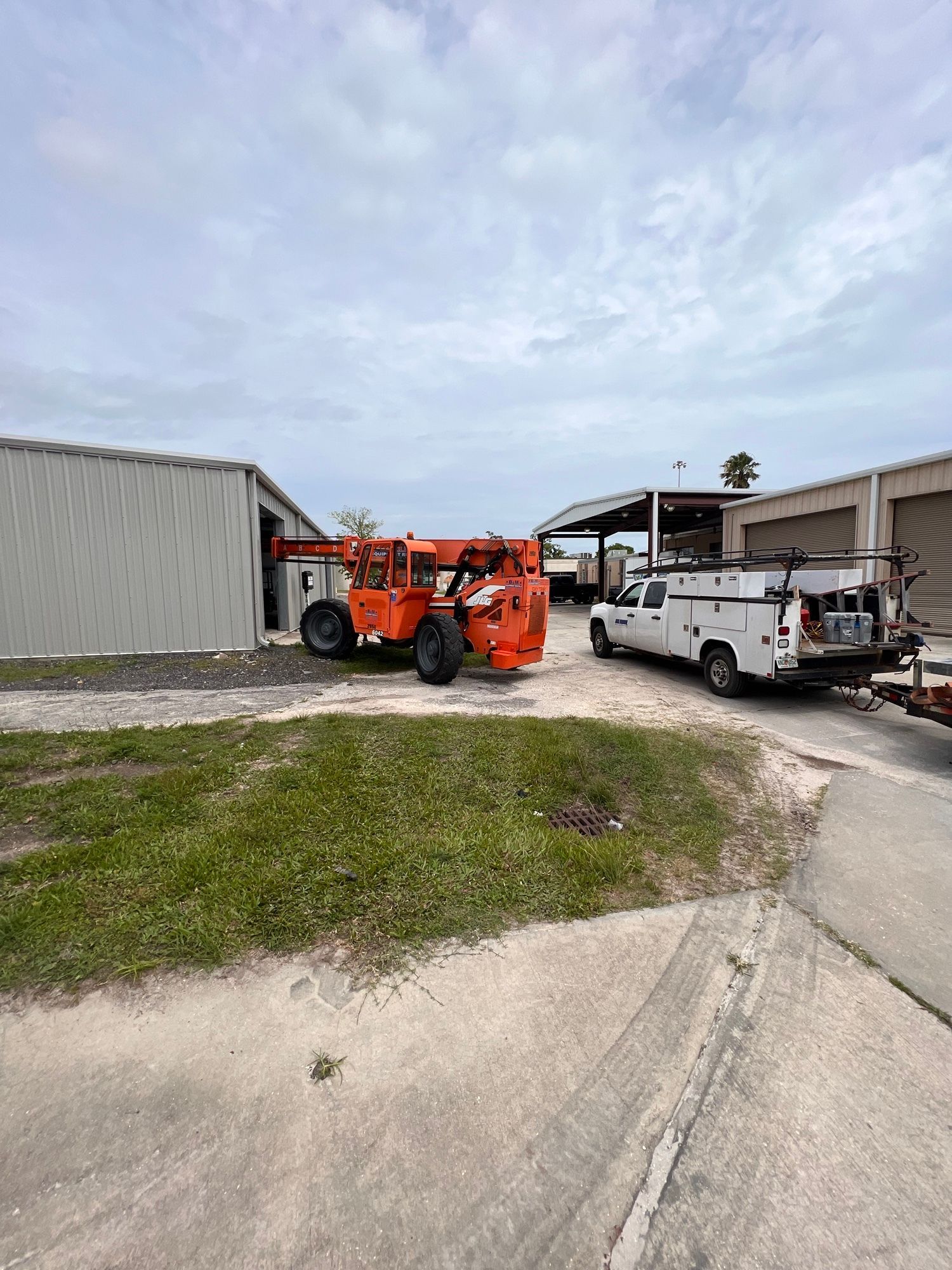 Orange lift next to a white truck with a trailer and a storage building under a cloudy sky.