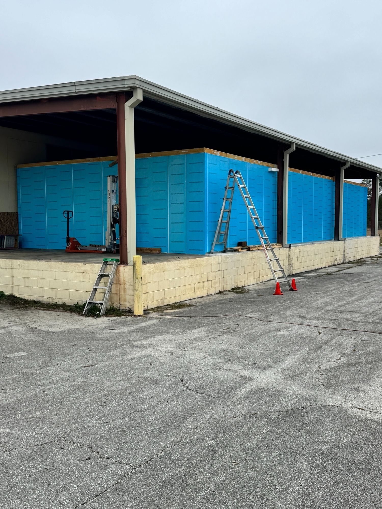 Building exterior with blue insulation panels, a ladder, and construction tools.