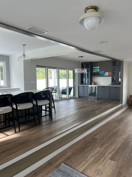 Open-concept kitchen and dining area with gray cabinetry, a bar, and wood flooring. Light streams through glass doors.