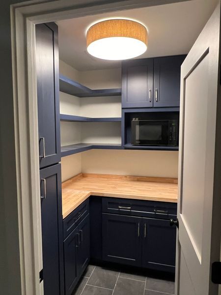 Blue pantry with wood countertops, open shelving, and a microwave.