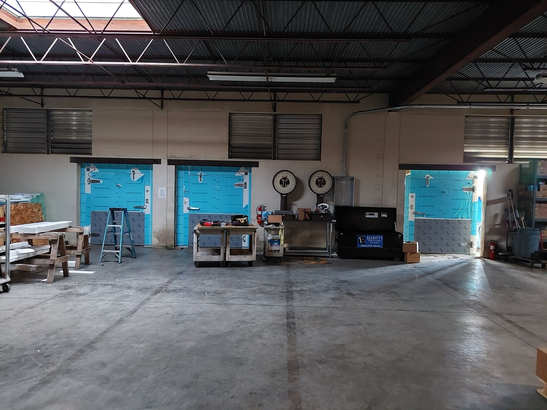 Large industrial warehouse interior with roll-up doors, various equipment, and skylight.