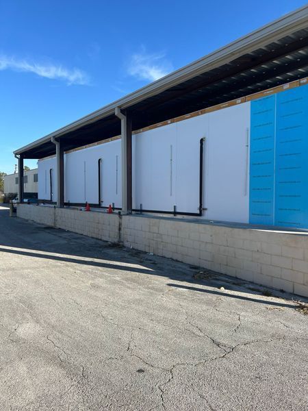 Loading dock with white and blue panels, beneath a dark roof. Concrete block base, blue sky.