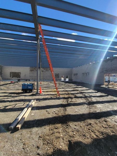 Construction site with steel beams, ladder, and dirt floor under a clear blue sky.