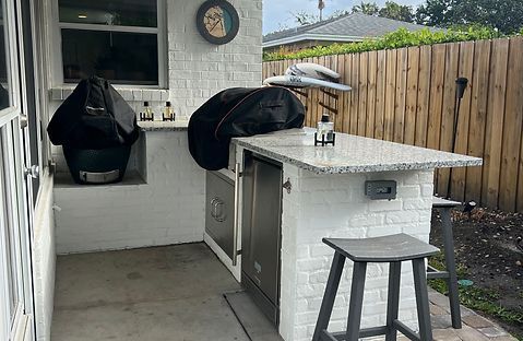 Outdoor kitchen with grill, refrigerator, bar, stools, and painted brick.