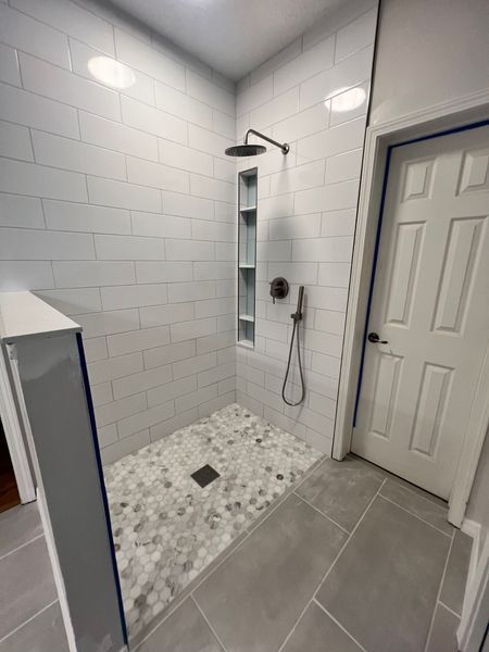 Bathroom with white subway tile shower, pebble floor, built-in shelf, and gray tile floor. Door on the right.