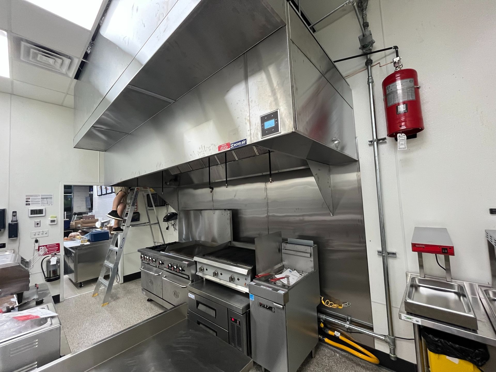 Commercial kitchen with stainless steel range hood, cooking equipment, and fire suppression system.