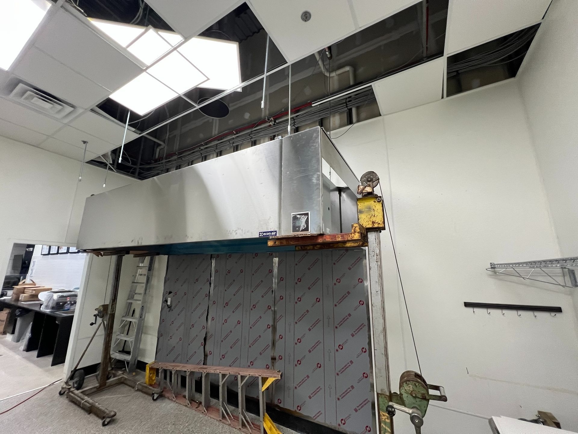 Construction site with a partially built stainless steel structure; ceiling panels and wires visible.