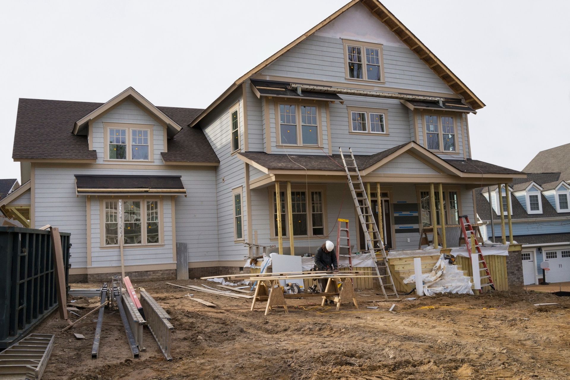 House under construction with worker cutting wood on a sawhorse in front.