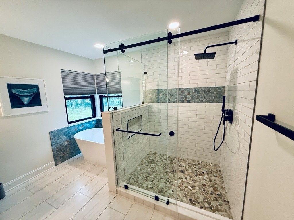 Modern bathroom with a glass shower, white and stone tile, and black fixtures.